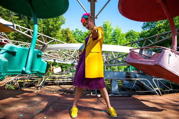 Sarı ceketli şık bir mankenin portresi lunaparkın arka planında poz veriyor. 