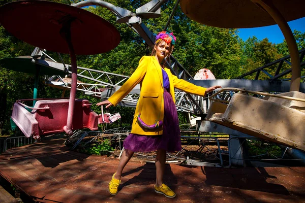 Sarı ceketli şık bir mankenin portresi lunaparkın arka planında poz veriyor. 