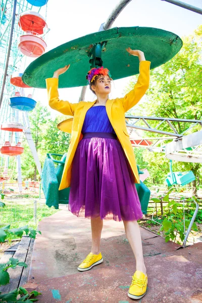 Sarı ceketli şık bir mankenin portresi lunaparkın arka planında poz veriyor. 