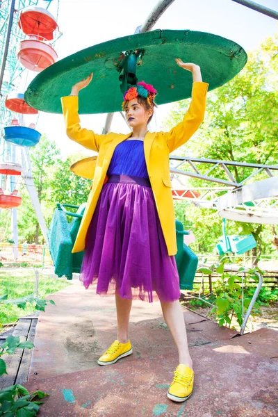 Sarı ceketli şık bir mankenin portresi lunaparkın arka planında poz veriyor. 
