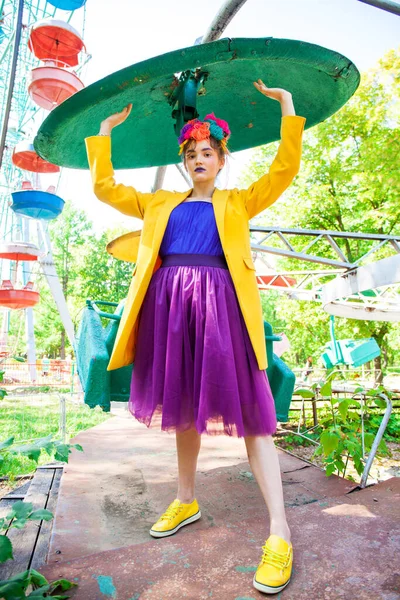 Sarı ceketli şık bir mankenin portresi lunaparkın arka planında poz veriyor. 