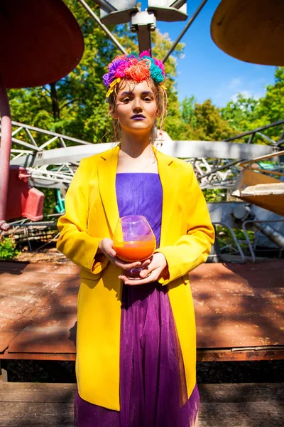 Sarı ceketli şık bir mankenin portresi lunaparkın arka planında poz veriyor. 