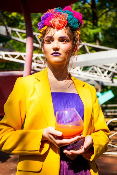 Sarı ceketli şık bir mankenin portresi lunaparkın arka planında poz veriyor. 