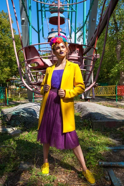 Sarı ceketli şık bir mankenin portresi lunaparkın arka planında poz veriyor. 