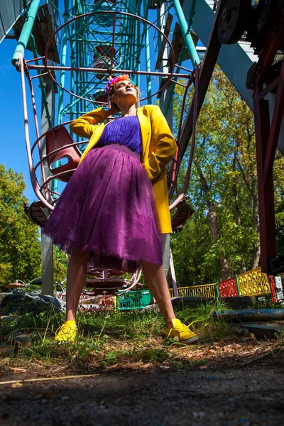 Sarı ceketli şık bir mankenin portresi lunaparkın arka planında poz veriyor. 