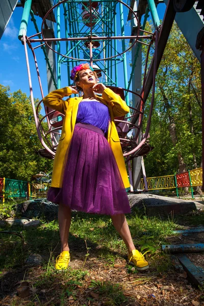 Sarı ceketli şık bir mankenin portresi lunaparkın arka planında poz veriyor. 