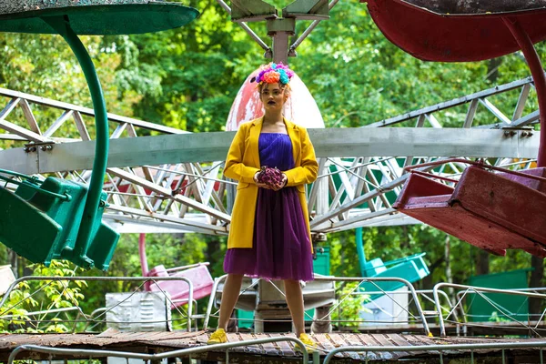 Sarı ceketli şık bir mankenin portresi lunaparkın arka planında poz veriyor. 