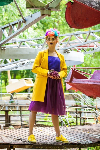 Sarı ceketli şık bir mankenin portresi lunaparkın arka planında poz veriyor. 