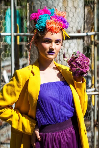 Sarı ceketli şık bir mankenin portresi lunaparkın arka planında poz veriyor. 