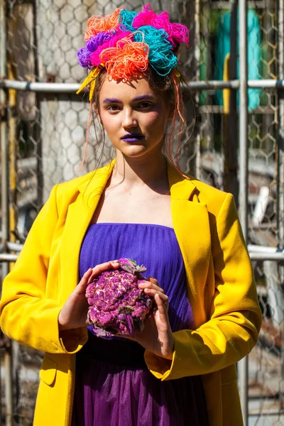 Sarı ceketli şık bir mankenin portresi lunaparkın arka planında poz veriyor. 