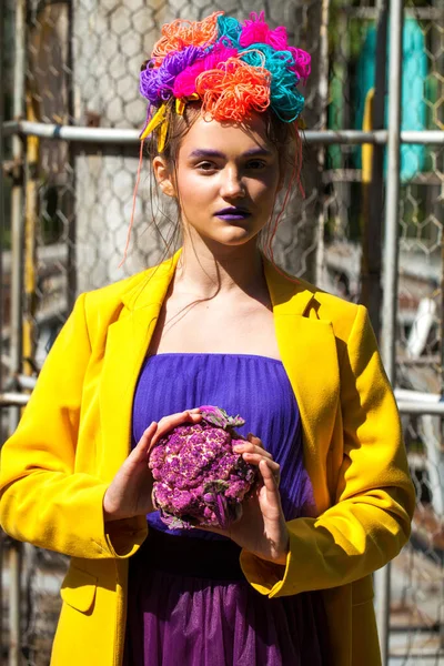 Sarı ceketli şık bir mankenin portresi lunaparkın arka planında poz veriyor. 