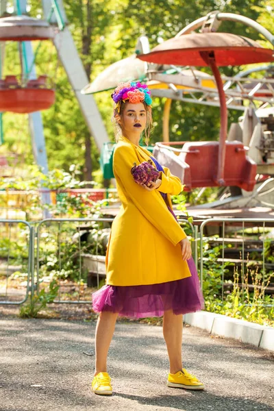 Güzel elbiseli genç bir kız eğlence parkının arka planında poz veriyor.