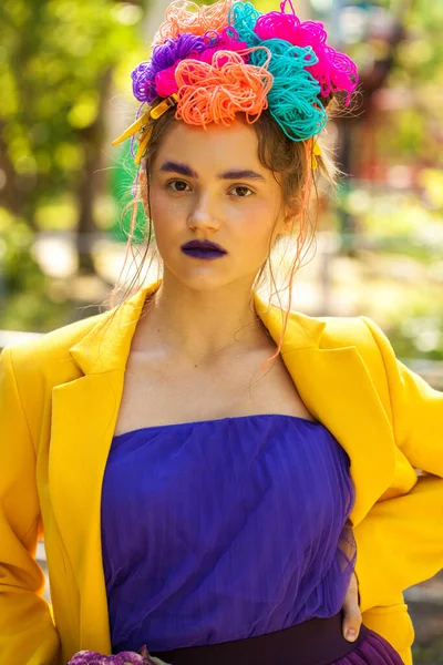 Güzel elbiseli genç bir kız eğlence parkının arka planında poz veriyor.