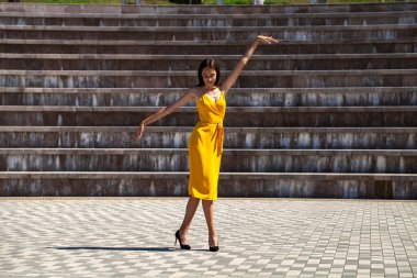 Sarı elbiseli, yaz parkında yürüyen sarışın bir kadının vücut portresi.