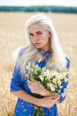 Bir tarlada bir buket papatya ile genç sarışın bir kızın portresini yakından çek.