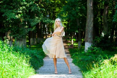 Açık hava parkında bej elbiseli güzel bir sarışının vücut portresi.