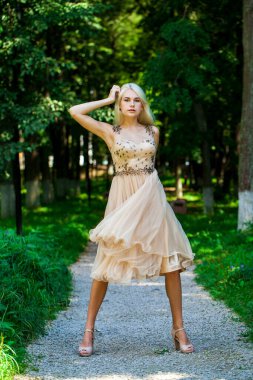 Açık hava parkında bej elbiseli güzel bir sarışının vücut portresi.