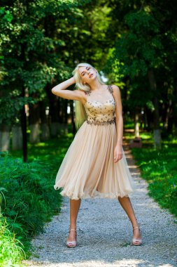 Açık hava parkında bej elbiseli güzel bir sarışının vücut portresi.