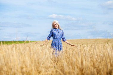 Mavi elbiseli, buğday tarlasında poz veren genç, güzel sarışın.