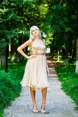 Açık hava parkında bej elbiseli güzel bir sarışının vücut portresi.
