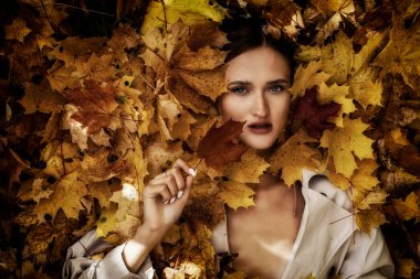 Genç ve güzel bir kadının sonbahar yapraklarında yatan portresi.