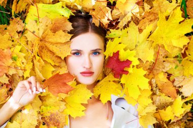 Genç ve güzel bir kadının sonbahar yapraklarında yatan portresi.