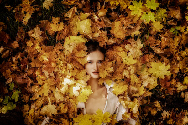 Top view portrait of young beautiful woman lying in autumn leaves