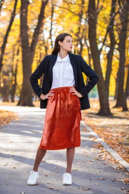 Sonbahar parkında yürüyen turuncu etekli esmer bir kadının vücut portresi.