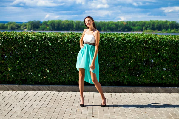 一个身材苗条的年轻貌美的姑娘 身穿蓝绿色的连衣裙 在堤岸上摆姿势 她的全长画像 — 图库照片