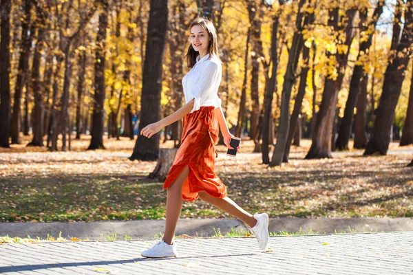 全身肖像画の若いですブルネット女性でオレンジ色のスカート歩くと秋の公園 — ストック写真