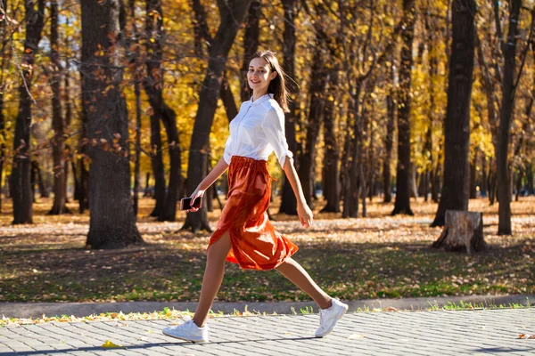 一个穿着橙色裙子在秋天公园散步的年轻黑发女子的全身像 — 图库照片