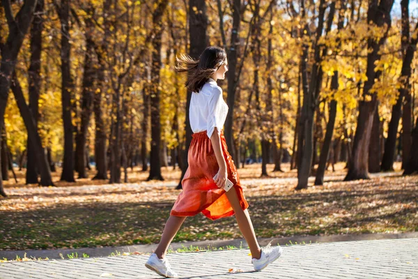 一个穿着橙色裙子在秋天公园散步的年轻黑发女子的全身像 — 图库照片