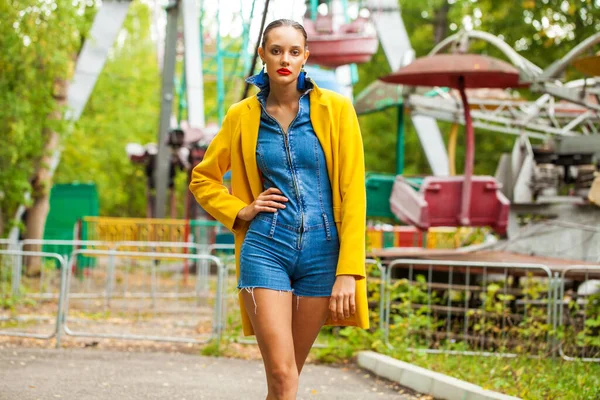 Modemodel Gelbem Mantel Und Jeanshose Posiert Auf Karussellhintergrund Einem Freizeitpark — Stockfoto