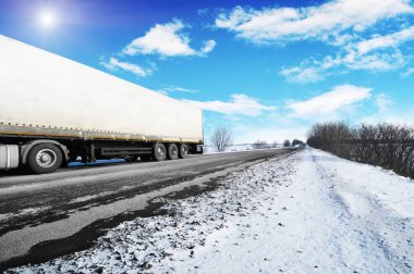 Beyaz kamyon ve beyaz bir römork ile olan mavi gökyüzü bulutlar ve parlak güneş kar kış kırsal yol üzerinde metin için yer