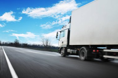 White truck driving fast and a white trailer with space for text on the countryside road against blue sky with clouds clipart