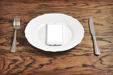 Beyaz perdeye sahip olan gümüş tabakta ve koyu ahşap arka plan üzerinde çatalı ile beyaz smartphone