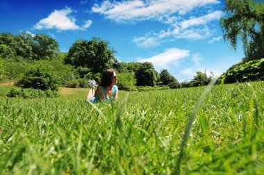 Güneş gözlüğü ağaçlar ile park ve mavi gökyüzü bulutlar ve güneş ile yeşil çimenlerin üzerinde rahatlatıcı genç kadın portresi
