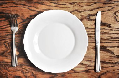 Beyaz porselen tabak, gümüş çatal ve bıçak koyu ahşap arka plan üzerinde