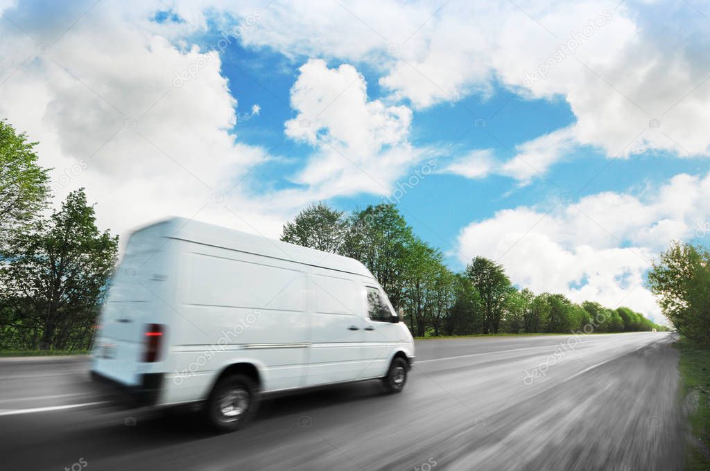 Big white van in motion on the countryside road shipping goods against blue sky with clouds