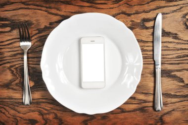Beyaz perdeye sahip olan gümüş tabakta ve koyu ahşap arka plan üzerinde çatalı ile beyaz smartphone