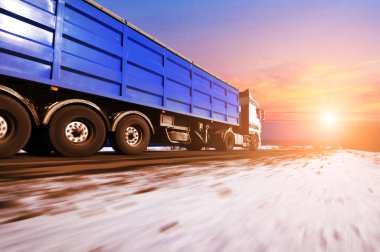 Beyaz kamyon ve kar bulutlar ve parlak günbatımı ile mavi gökyüzü ile kış kırsal yolda hızlı sürüş metin için yer ile mavi römork