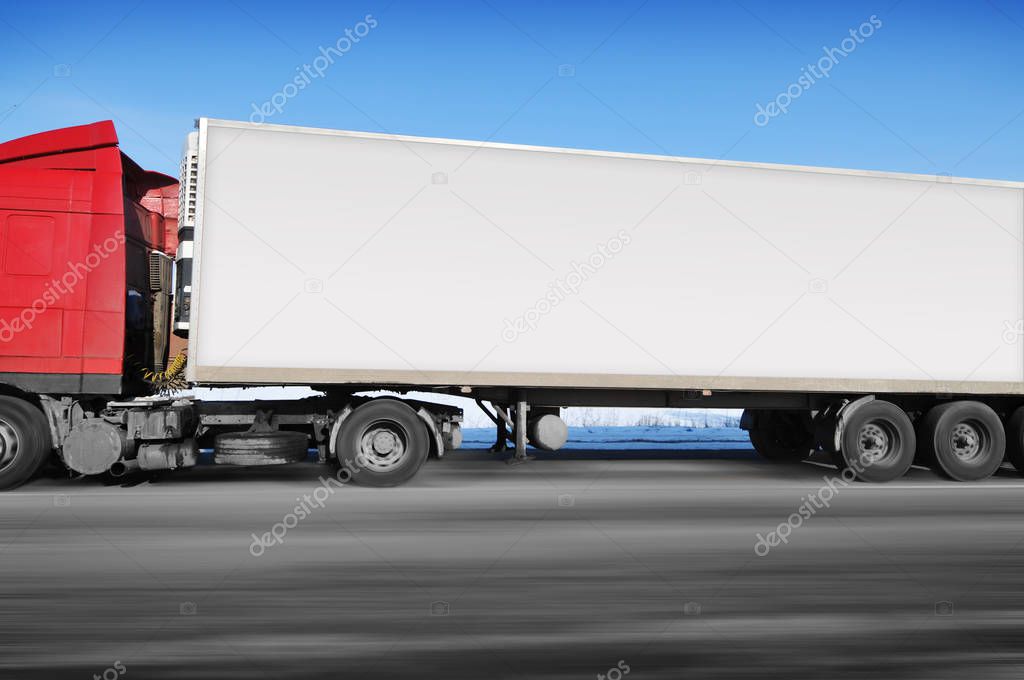 Red truck and white trailer with space for text driving fast on winter countryside road with snow against blue sky