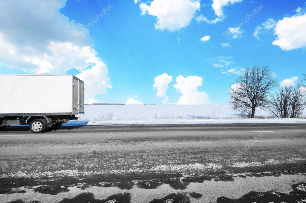 White box truck on countryside winter road with snow against blue sky with clouds