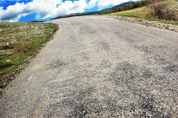 Empty countryside road with grass and forest against blue sky with white clouds