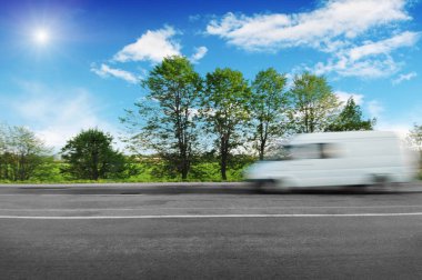 Bulanık beyaz büyük van yeşil ağaçlar ve çalılar mavi gökyüzü bulutlu karşı kırsal yolda hızlı sürüş