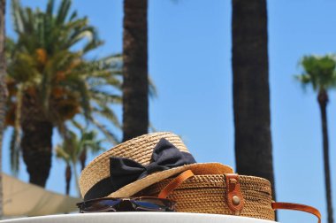 Yuvarlak hasır çanta, hasır şapka ve palmiye ağaçları ve mavi gökyüzü arka plan üzerinde siyah güneş gözlüğü