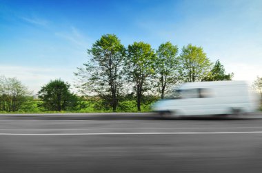 Hızlı hareket yeşil ağaçlar ve çalılar mavi gökyüzü ile kırsal yolda sürüş beyaz büyük van
