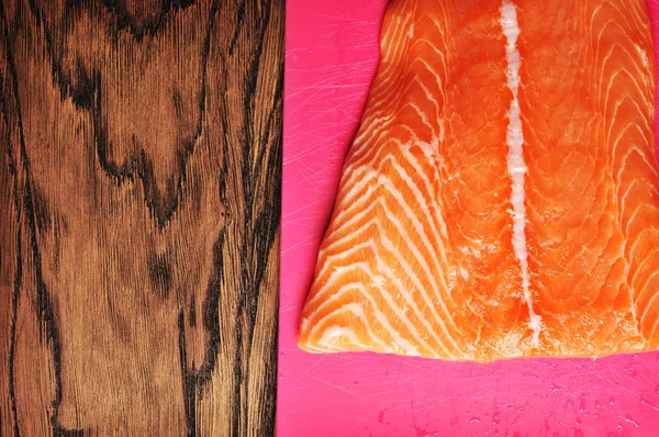 木桌上粉红色塑料切菜板上的新鲜橙色三文鱼片 — 图库照片