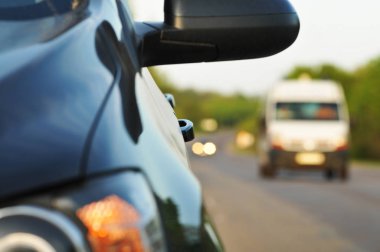 Blcak araba yan ayna ve yeşil ağaçlar ve gökyüzü ile kırsal yolda araba ile bulanık arka plan