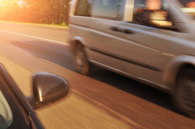 Siyah araba yan ayna ve diğer araba güneş ışığı ile akşam yeşil ağaçlar ile hareket kırsal yolda hızlı sürüş